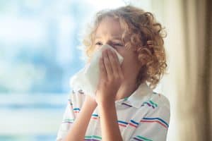 Picture of a young boy sneezing into a tissue.