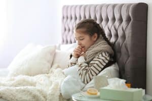 Picture of a young girl with RSV sitting up in bed and coughing.