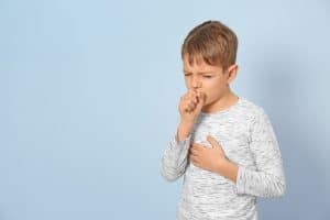Picture of a young boy with RSV standing and coughing in front of a light blue background.