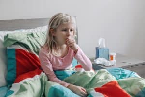 Picture of a young girl with RSV sitting in bed and coughing.