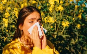 Picture of a woman sneezing into a tissue because she's having an allergic reaction to flowers.