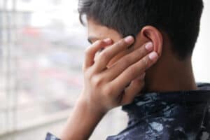Picture of a man who requires ear wax removal touching his ear in pain.