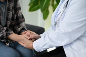 Picture of a doctor holding a patient's hands and comforting them while discussing a medication-assisted opioid treatment program.