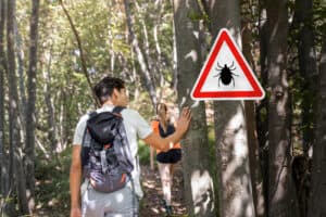 Picture of hikers walking past a tick warning sign in a forest.