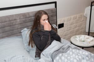 Picture of a sick woman sitting in bed and blowing her nose into a tissue.