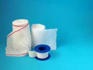 Picture of rolls of gauze and medical tape against a blue background.