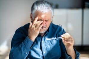 Picture of a man taking off his glasses and touching his eye in pain because he needs pink eye treatment.