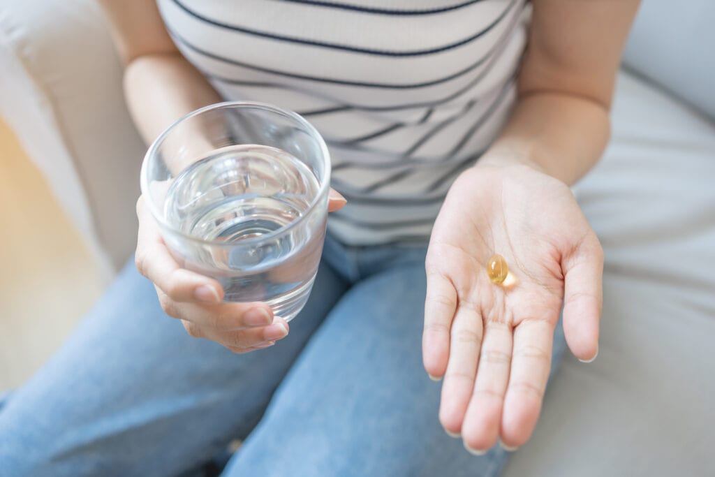 Picture of a woman sitting on a couch and holding a glass of water and a daily multivitamin.