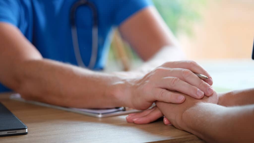 Picture of a medical provider holding a patient's hands over a desk to comfort them as they discuss drug addiction treatment.