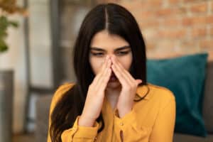 Picture of a woman wincing and holding the sides of her nose because she's experiencing sinus infection pain.