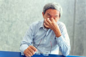 Picture of a man with a sinus infection taking off his glasses and holding the bridge of his nose in pain.